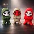 Three toy figures with hooded outfits in green, beige, and red on a dark surface.